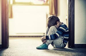 Niño triste y deprimido sentado en el suelo, en la puerta. El niño esconde la cabeza entre las piernas.