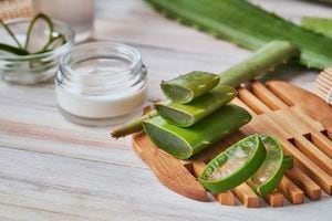 Aloe vera slices and moisturizer on a wooden table. Beauty treatment concepts