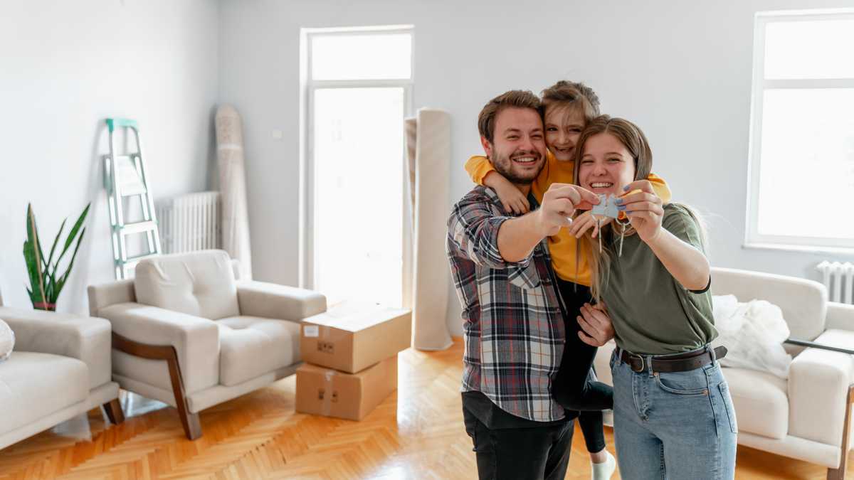 Una familia joven estadounidense emocionada muestra las llaves de su propia casa, una pareja feliz que compra la primera casa juntos, un esposo y una esposa sonrientes compran una nueva propiedad. Concepto de propiedad