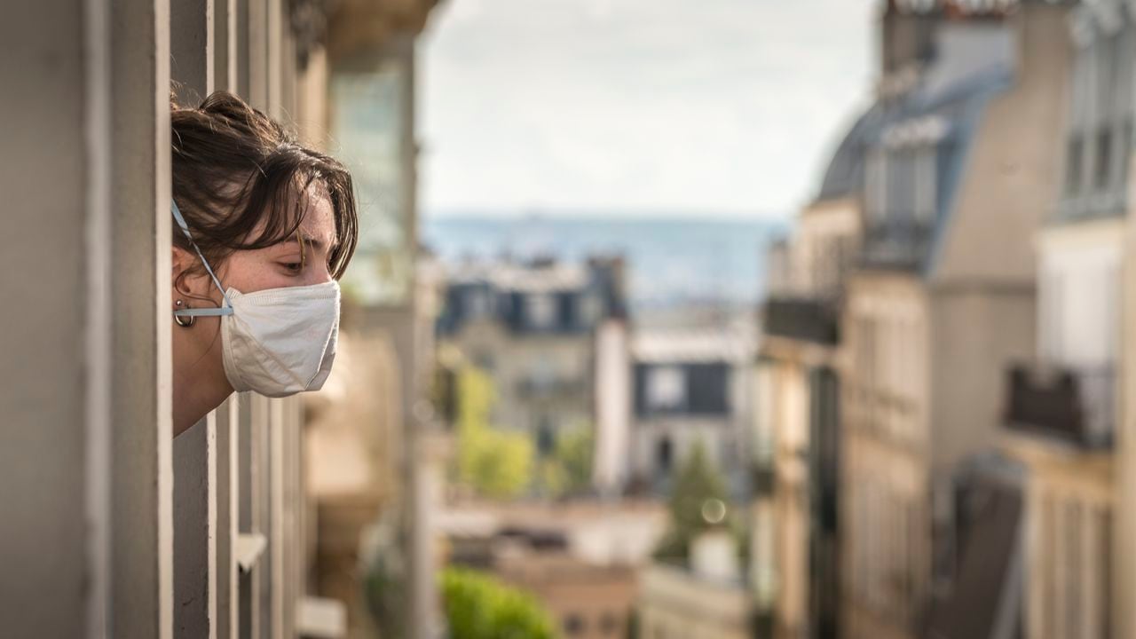 Una parisina con tapabocas mira por la ventana