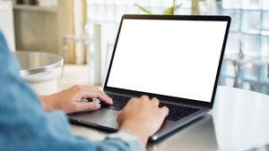 una mujer que usa y escribe en una computadora portátil con una pantalla de escritorio en blanco