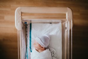 Un bebé recién nacido en el hospital descansa en una cuna de bassinet de hospital, envuelta en un swaddle y con un sombrero de gorro.