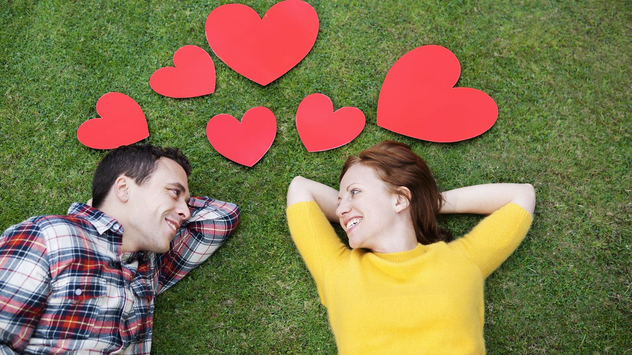 Couple laying in grass,surrounded by hearts.