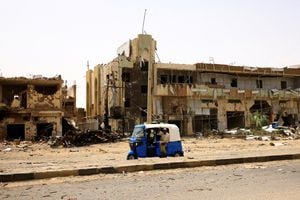 La gente pasa por automóviles y edificios dañados en el mercado central durante los enfrentamientos entre las Fuerzas paramilitares de apoyo rápido y el ejército en Jartum Norte, Sudán, 27 de abril de 2023. 