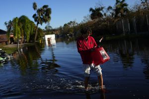 José Cruz, de 13 años, lleva un bidón vacío a través de las aguas de inundación que retroceden frente a su casa mientras su familia sale a buscar suministros, tres días después del paso del huracán Ian, en Fort Myers, Florida