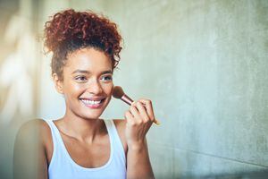 Shot of a young woman using a makeup brush while looking in her bathroom mirror