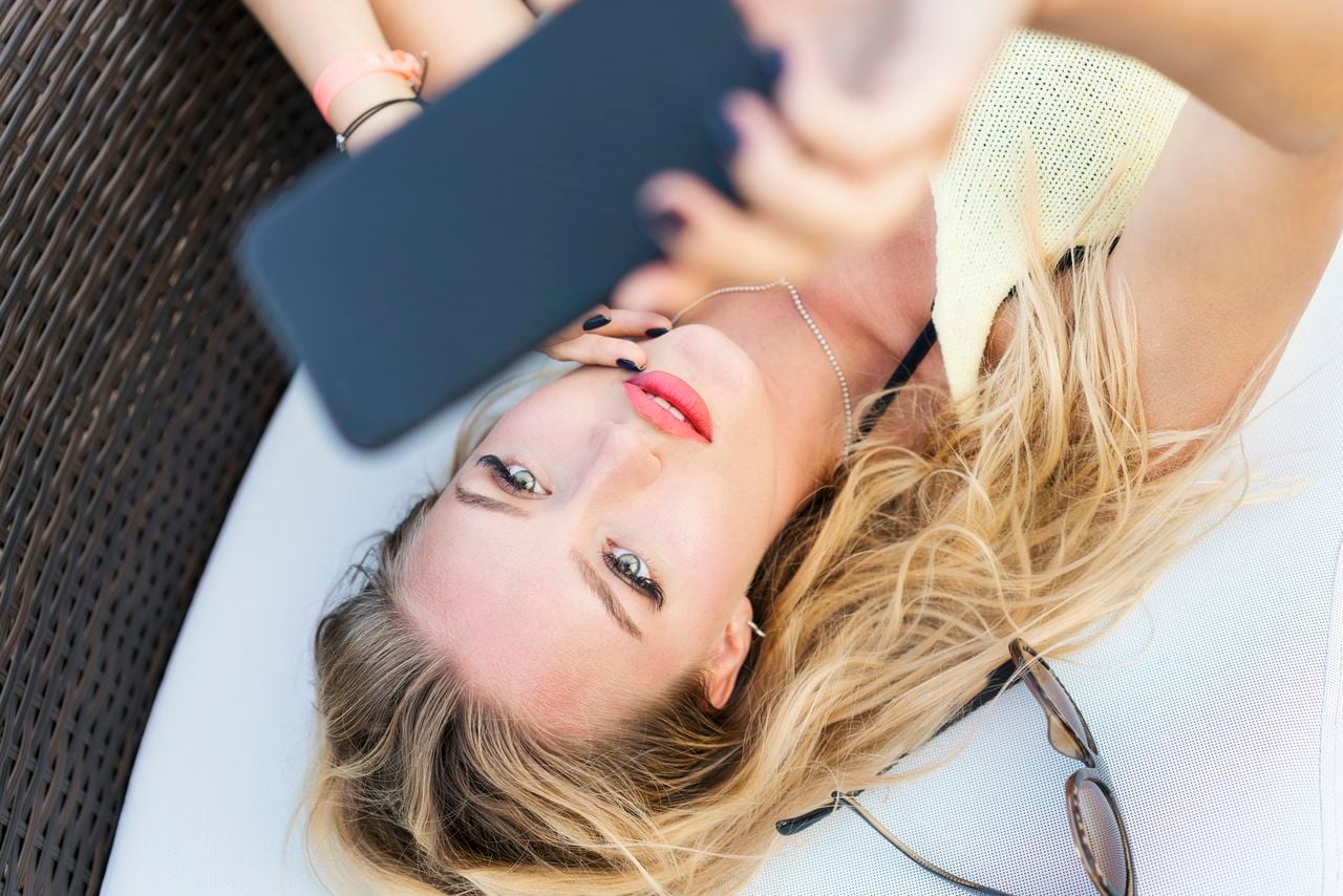 Mujer joven sensual que hace la foto en su teléfono inteligente mientras está acostado en la playa Webcam