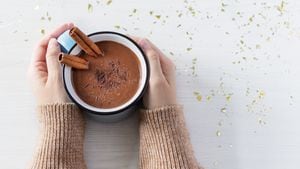Chocolate caliente con especias de canela en una taza de esmalte en manos femeninas en la vista superior de fondo blanco de madera. Bebida caliente y acogedora para la temporada de otoño o invierno.