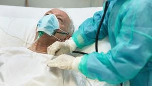 Vista parcial de la enfermera con ropa protectora escuchando los sonidos del pecho de un paciente varón caucásico de 64 años acostado en la cama del hospital.
