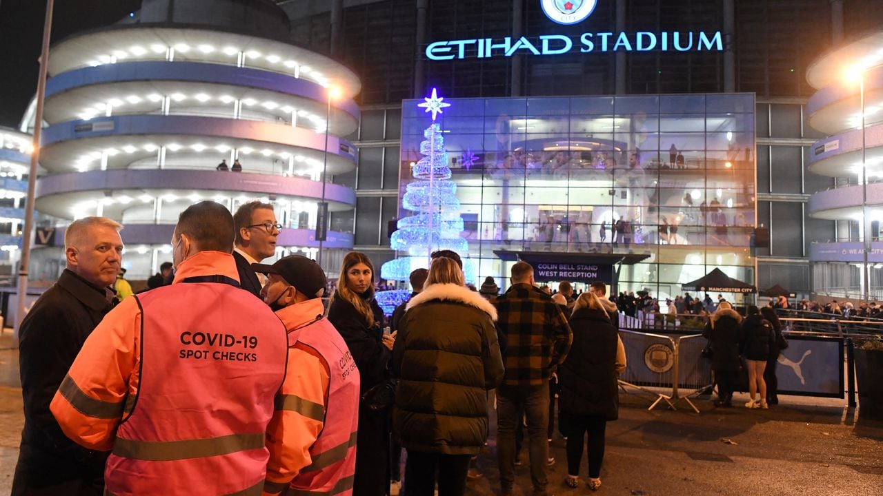 Stewards check fans' covid passports or negative lateral flow test results, as they queue to enter the stadium ahead of the English Premier League football match between Manchester City and Leeds at the Etihad Stadium in Manchester, north west England, on December 14, 2021. (Photo by Paul ELLIS / AFP) / RESTRICTED TO EDITORIAL USE. No use with unauthorized audio, video, data, fixture lists, club/league logos or 'live' services. Online in-match use limited to 120 images. An additional 40 images may be used in extra time. No video emulation. Social media in-match use limited to 120 images. An additional 40 images may be used in extra time. No use in betting publications, games or single club/league/player publications. /