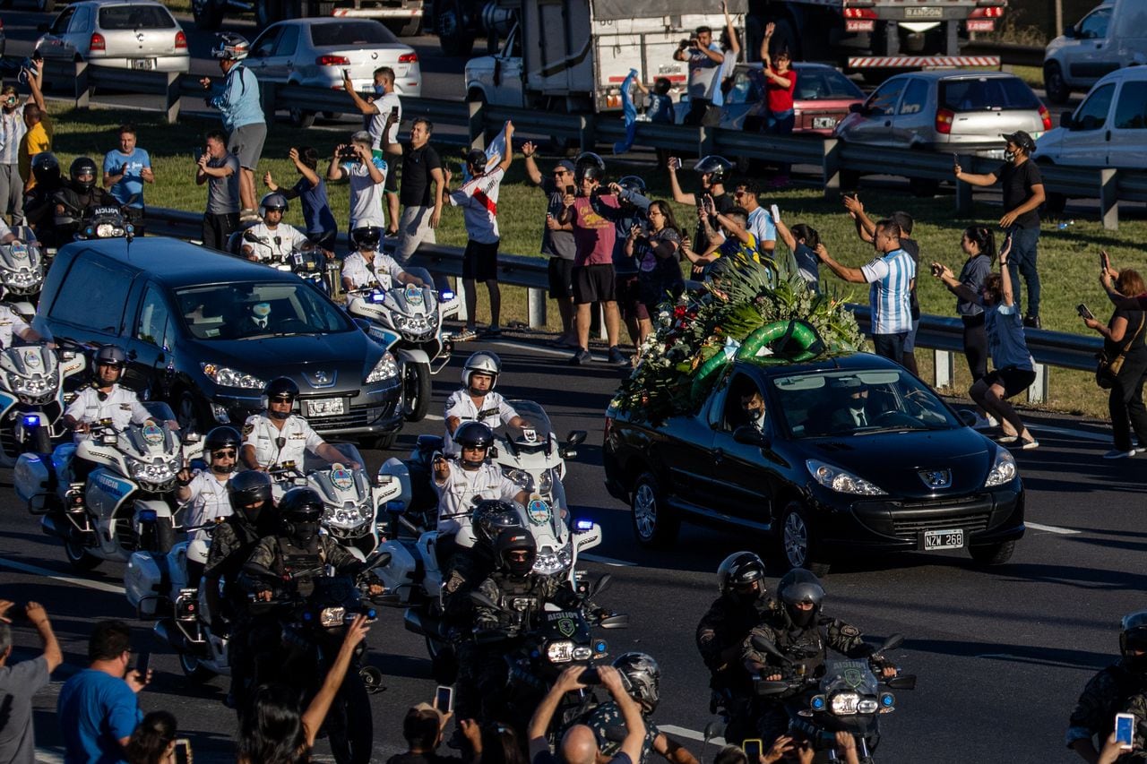 Los fanáticos al costado de la carretera animan al coche fúnebre que lleva el cuerpo de Diego Maradona que lo transporta por la Carretera 25 de Mayo al Jardín de Bella Vista antes de la ceremonia de entierro el 26 de noviembre de 2020 en Bellavista, Buenos Aires, Argentina