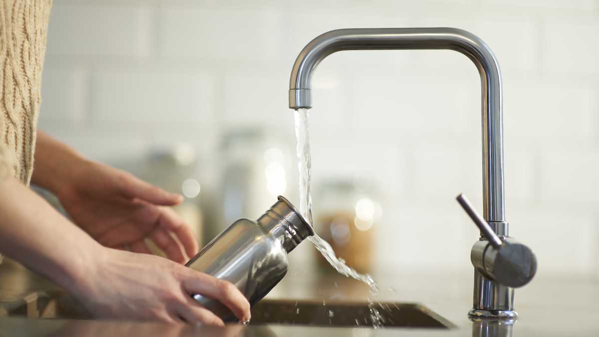 Una mujer limpia una botella de agua reutilizable y sin plástico en el fregadero de la cocina, de cerca.