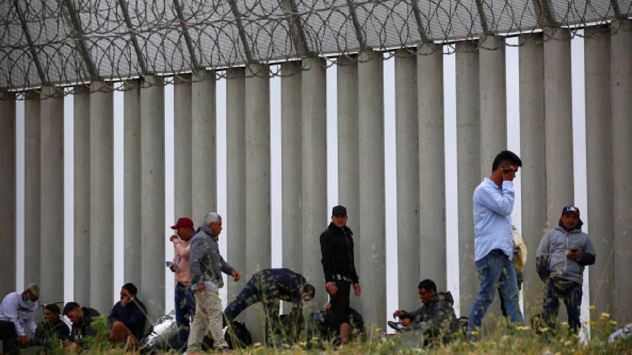Migrantes llegan a la frontera para pedir asilo a autoridades estadounidenses entre los muros fronterizos.