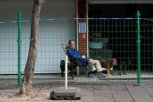 Un hombre se sienta con tres perros detrás de una barrera en un área sellada tras el brote de la enfermedad por coronavirus (COVID-19), en Shanghái, China, el 11 de octubre de 2022. 
