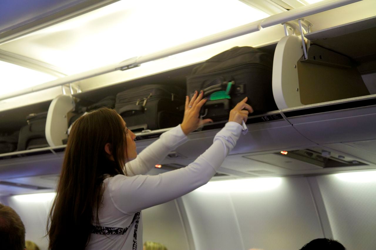 Una mujer pone su equipaje de mano en el compartimiento del avión