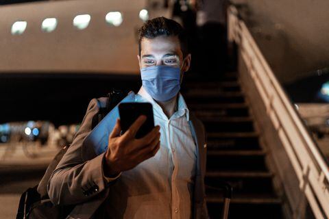 Empresario mediante teléfono móvil en el aeropuerto con máscara protectora