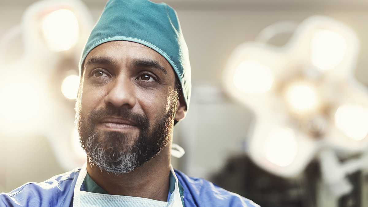 Cirujano de sexo masculino barbudo mirando a otro lado. El doctor está trabajando en quirófano iluminado. Lleva uniformes médicos.