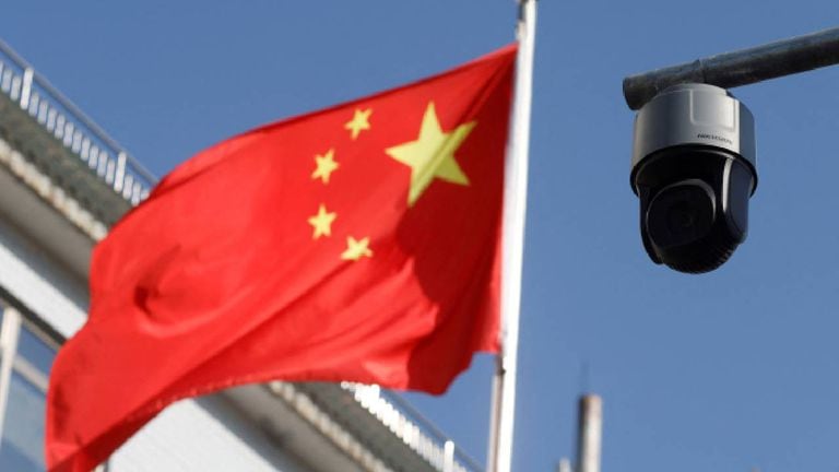 Una cámara de vigilancia de seguridad con vista a una calle junto a una bandera de China que ondea cerca en Beijing.