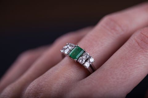 Close up of an emerald ring in woman finger, with diamonds and platinum. Studio shot, black background.