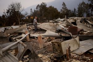 Julio Escobar works on cleaning the debris of his house, that was destroyed after a fire, in Tome, Chile, Saturday, Feb. 4, 2023. Forest fires are spreading in southern and central Chile, triggering evacuations and the declaration of a state of emergency in some region. (AP Photo/Matias Delacroix)