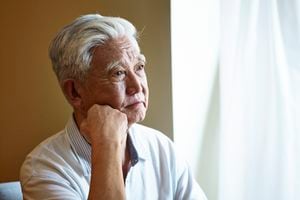 Retrato de un hombre mayor asiático triste sentado junto a la ventana con la mano en la barbilla.