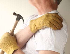 a man grasps his aching shoulder while holding a hammer with his other hand