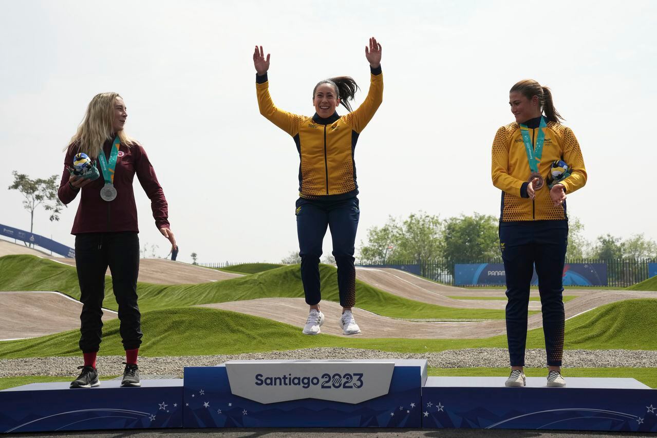 Gold medal winner, Colombia's Mariana Pajon, center, jumps to the podium of the Women's BMX Racing as fellow medalists Canada's Molly Simpson, left, and Colombia's Gabriela Bolle look at her at the Pan American Games in Santiago, Chile, Sunday, Oct 22, 2023. (AP Photo/Dolores Ochoa)