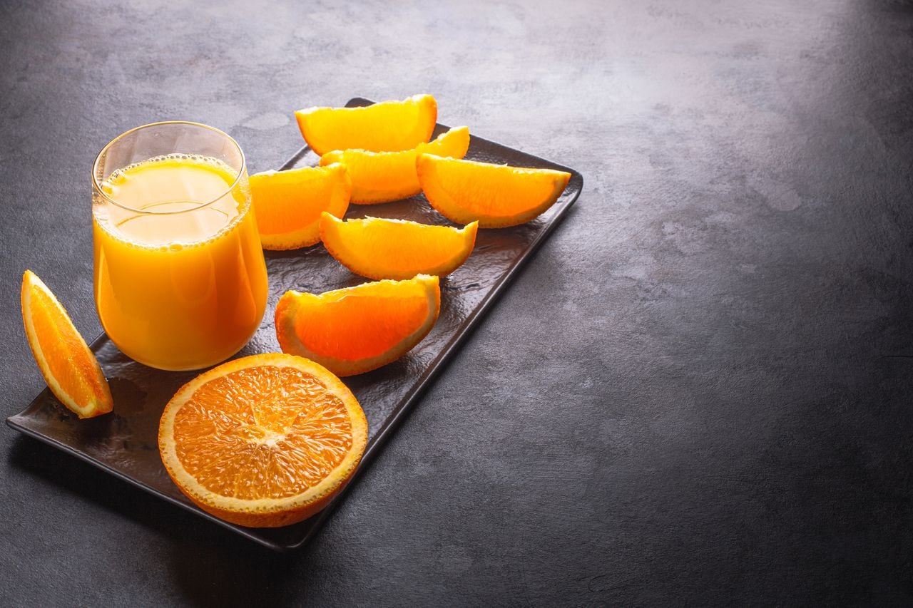Orange juice and sliced oranges on dark plate and black background, back lit.