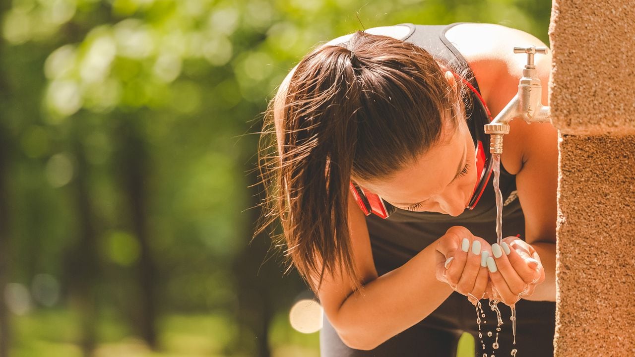 Mujer toma agua de grifo después de hacer ejercicio.
