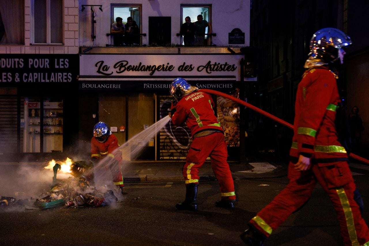 Los bomberos extinguen un incendio luego de un concierto de panes para protestar durante el discurso televisado a la nación del presidente francés Emmanuel Macron, luego de promulgar una ley de reforma de las pensiones, en París el 17 de abril de 2023. (Foto de Geoffroy Van der Hasselt / AFP)