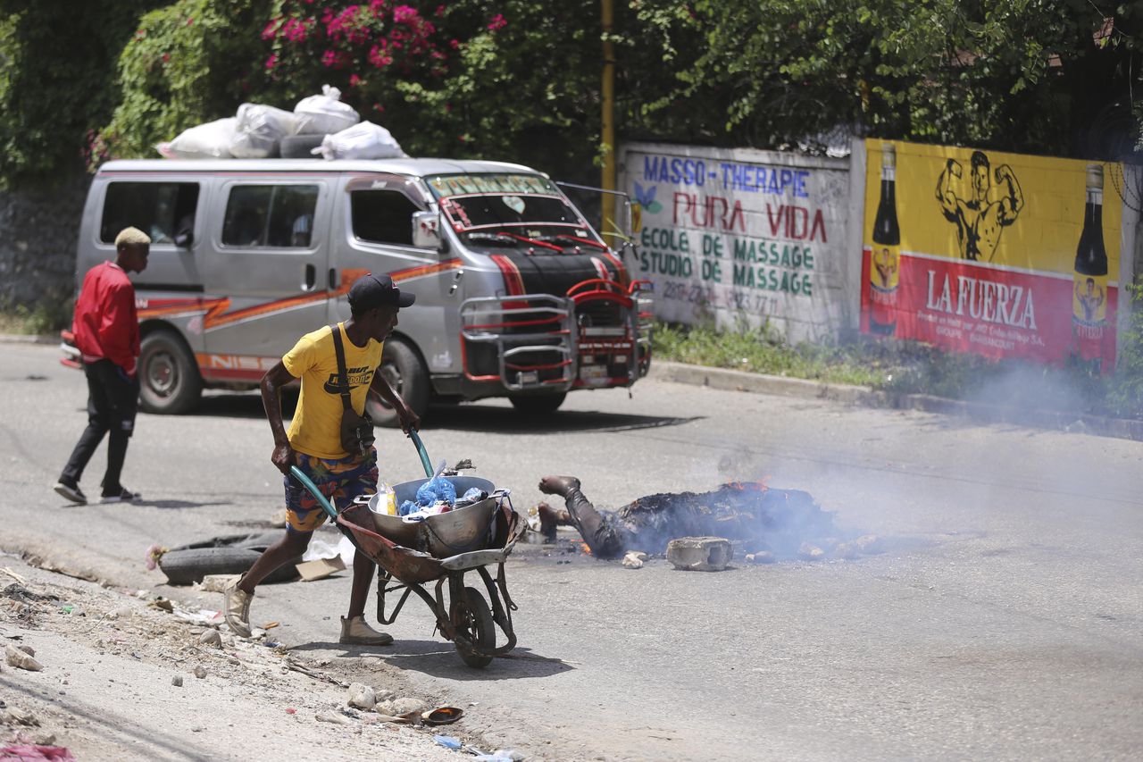 La gente pasa junto al cuerpo de un hombre acusado de robar una motocicleta que fue asesinado e incendiado en el barrio de Petion-ville de Port-au-Prince, Haití