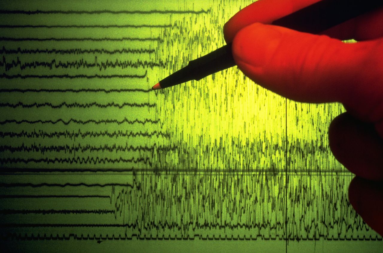 A seismographer uses a pen to point out the initial shock waves of an earthquake charted on a seismograph.