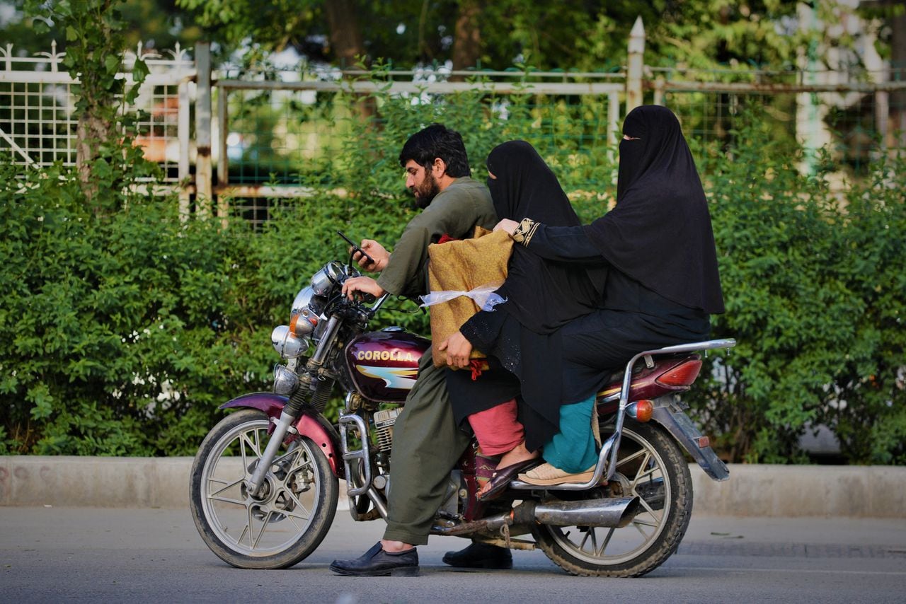 Mujeres vestidas con niqab sentadas en una motocicleta con un pariente antes de recorrer una carretera en Kabul el 7 de mayo de 2022. - El 7 de mayo, los talibanes impusieron algunas de las restricciones más duras a las mujeres de Afganistán desde que tomaron el poder y les ordenaron cubrirse. totalmente en público, idealmente con el burka tradicional. (Foto de Ahmad SAHEL ARMAN / AFP)