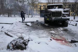 The body of a serviceman is coated in snow as a man takes photos of a destroyed Russian military multiple rocket launcher vehicle on the outskirts of Kharkiv, Ukraine, Friday, Feb. 25, 2022. Russian troops bore down on Ukraine's capital Friday, with gunfire and explosions resonating ever closer to the government quarter, in an invasion of a democratic country that has fueled fears of wider war in Europe and triggered worldwide efforts to make Russia stop. (AP Photo/Vadim Ghirda)