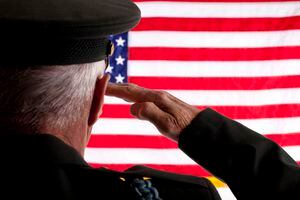 Senior adult veteran man in military dress uniform saluting the 50 star American flag.  