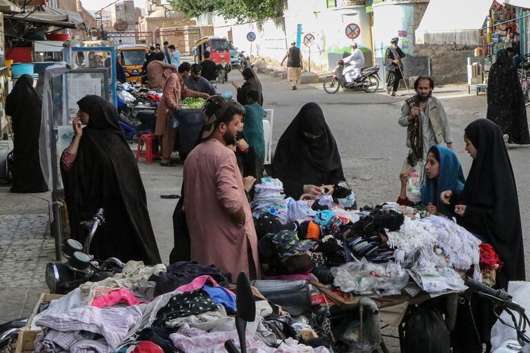 Las mujeres compran ropa en un puesto callejero en Herat el 7 de mayo de 2022. - El 7 de mayo, los talibanes impusieron algunas de las restricciones más duras a las mujeres de Afganistán desde que tomaron el poder, y les ordenaron cubrirse por completo en público, idealmente con el burka tradicional. (Foto de Mohsen KARIMI / AFP)