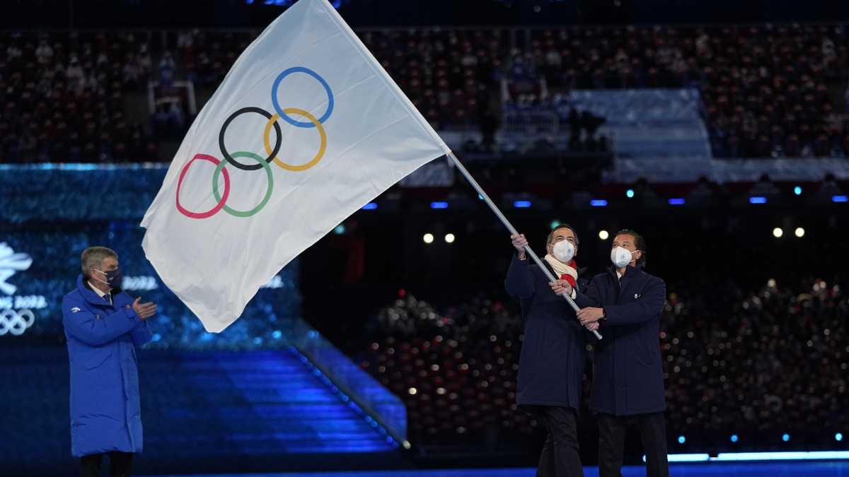 El alcalde de Milán Giuseppe Sala y el Cortina Gianpietro Ghedina (derecha) ondean la bandera olímpica frente al presidente del COI Thomas Bach durante la ceremonia de clasura de los Juegos Olímpicos de Invierno de Beijing, el domingo 20 de febrero de 2022. (AP/Jae C. Hong)