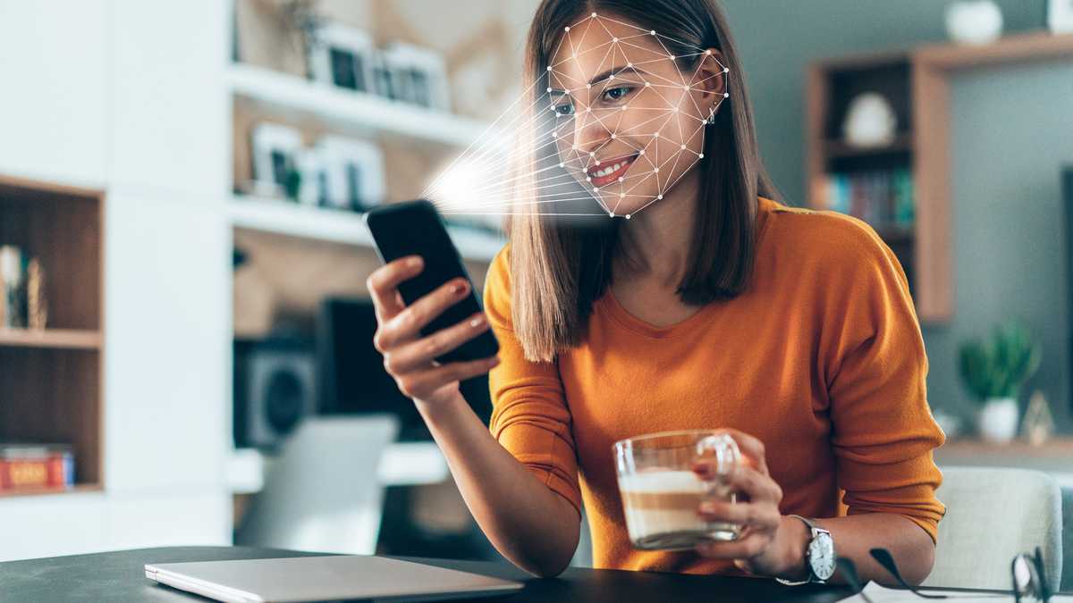 El software de reconocimiento facial escanea el rostro de una mujer joven que sostiene un teléfono inteligente en casa