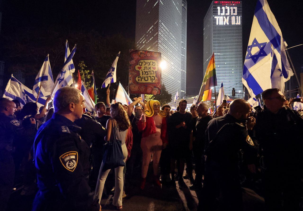 La gente sostiene banderas israelíes mientras bloquean una carretera durante una manifestación contra la reforma judicial del gobierno de coalición nacionalista de Israel, luego de un discurso televisado pronunciado por el primer ministro israelí Benjamin Netanyahu, en Tel Aviv