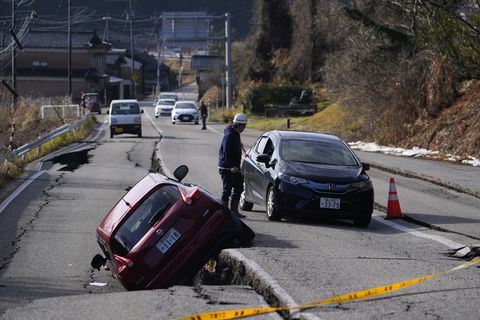 Un hombre dirige a un conductor que avanza por una calle dañada cerca de la ciudad de Anamizu en la península de Noto frente al Mar de Japón, al noroeste de Tokio, el martes 2 de enero de 2024