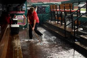 El asistente de la casa club de los St. Louis Cardinals, Andrew Rettig, intenta despejar un desagüe en el dugout inundado de los Cardinals durante un retraso por lluvia en el primer juego de una doble cartelera de béisbol entre los Cardinals y los New York Yankees