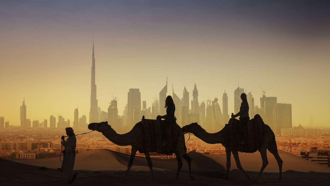 Turistas en camellos contemplando Dubái, unos de los uno de los siete emiratos que conforman los Emiratos Árabes Unidos