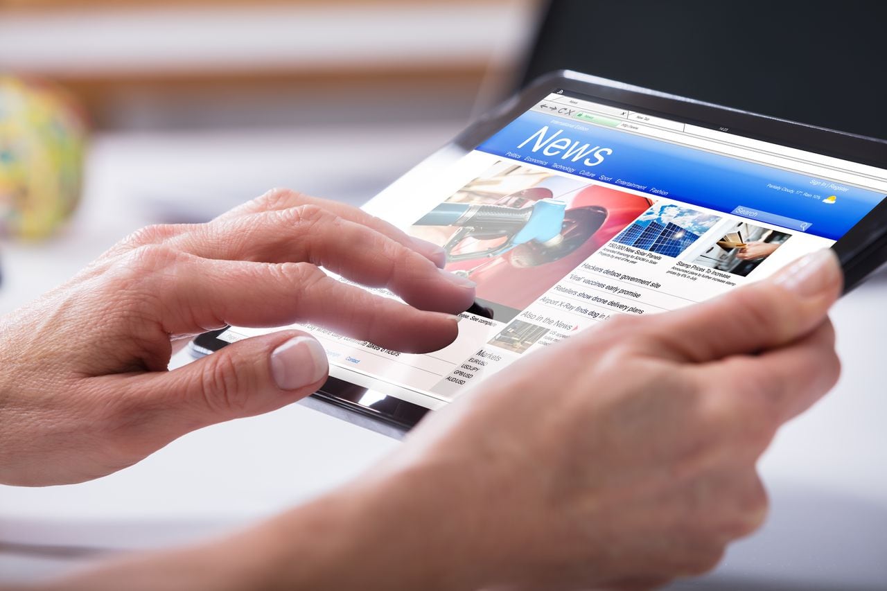 Close-up de la mano de una persona con tableta digital con pantalla que muestra noticias en línea