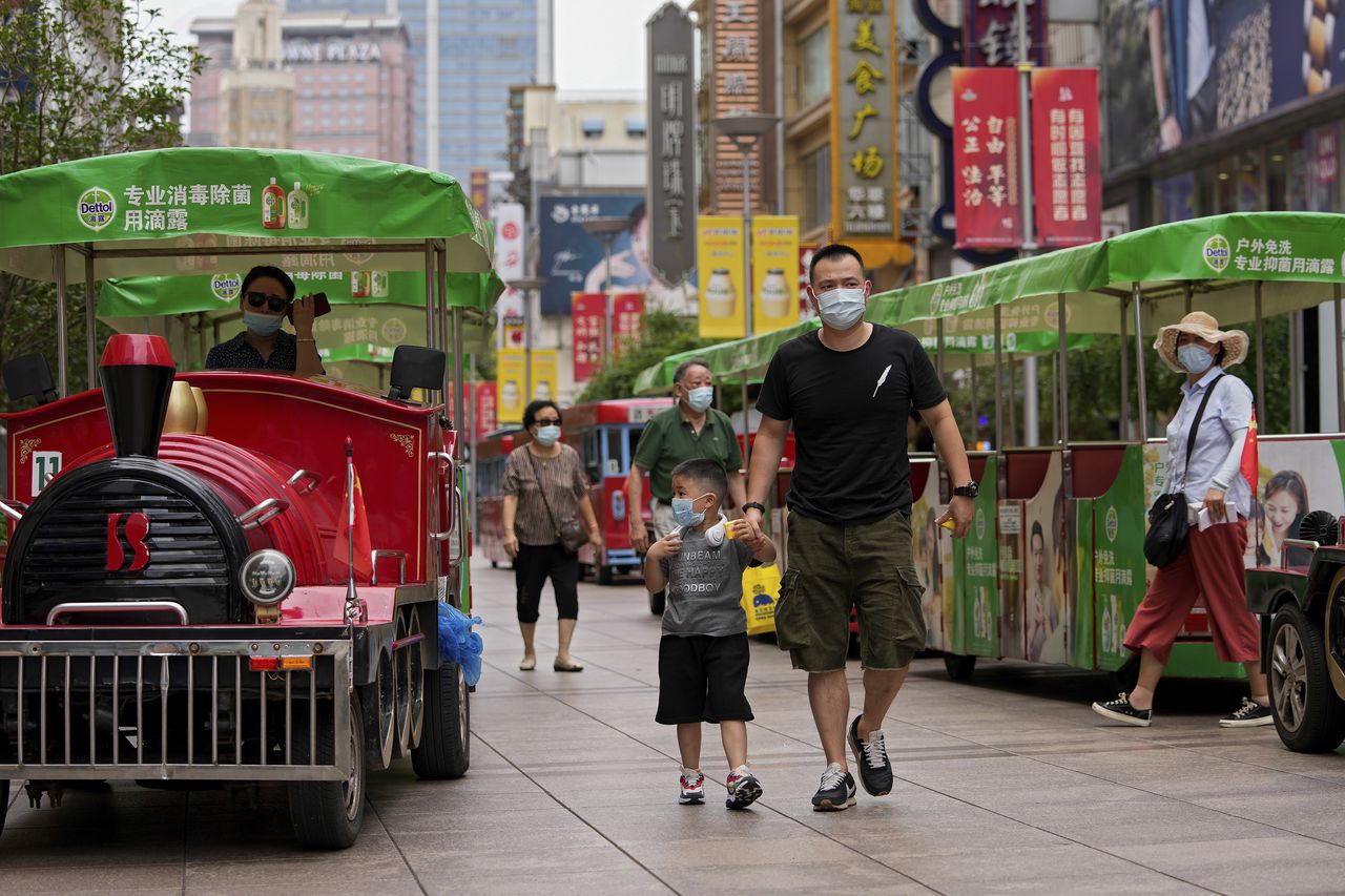 Personas que usan mascarillas para ayudar a frenar la propagación del coronavirus caminan en trenes de juguete a lo largo de una calle comercial en Shanghai, China, el lunes 23 de agosto de 2021 (AP Photo / Andy Wong).