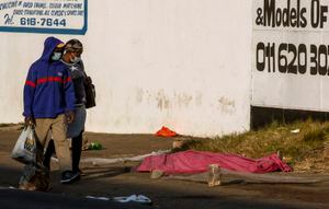A couple walks past a body covered with a blanket after protests in the area, in Johannesburg, South Africa, Sunday, July 11, 2021. Protests have spread from the KwaZulu Natal province to Johannesburg against the imprisonment of former South African President Jacob Zuma who was imprisoned last week for contempt of court. (AP Photo/Themba Hadebe)