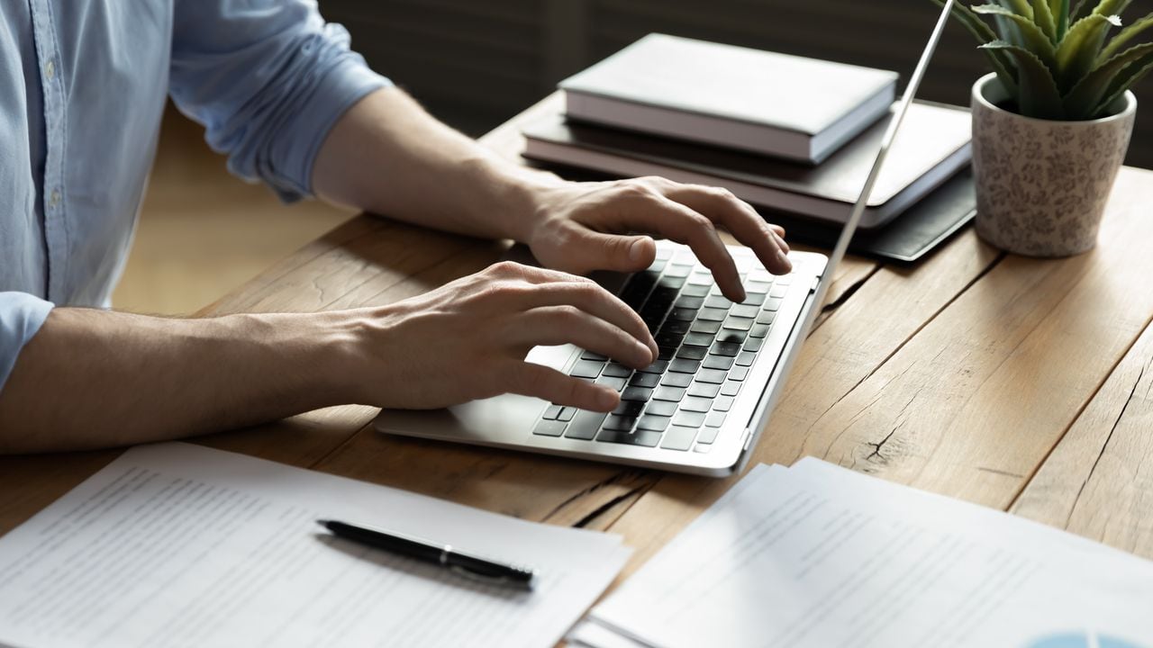 Hombre de negocios de cerca usando una computadora portátil, escribiendo en el teclado, sentado en un escritorio de madera con documentos, escribiendo un correo electrónico, contable escribiendo un informe financiero, estudiante ocupado estudiando en línea, buscando información
