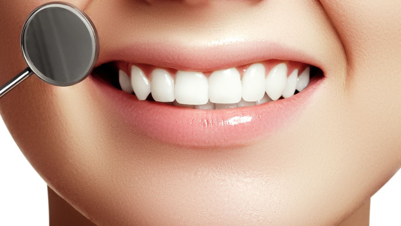 Woman's smile. Healthy white woman's teeth and a dentist mouth mirror closeup. Dental hygiene, oral care concept. Examination at dentistry with dental tools. Teeth whitening. Stomatology concept