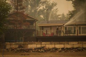 Trevor Manzuik, quien fue evacuado de su vivienda debido a un incendio forestal, rocía su propiedad luego de regresar a casa en bote, el domingo 20 de agosto de 2023, en la Columbia Británica, Canadá.