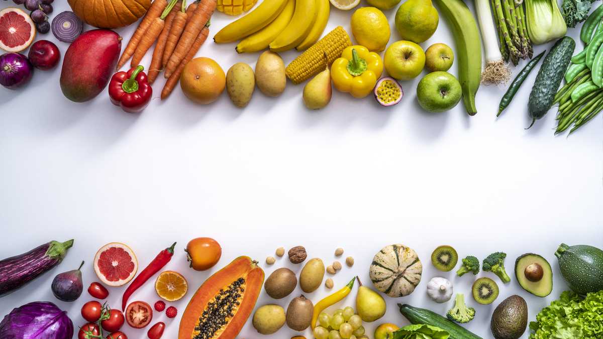 Coloridas verduras y frutas comida vegana en disposición de colores del arco iris dejando espacio de copia aislado en blanco