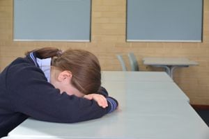 Sad young schoolgirl (female age 12-13) sitting alone in classroom after being bullied by students.